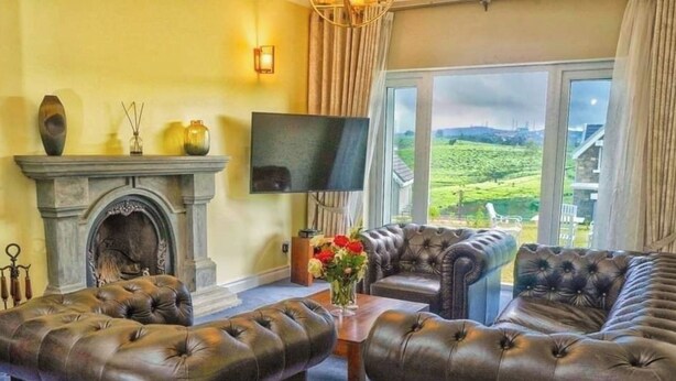 Una sala de estar con chimenea, sofás de cuero, televisor y vistas al campo.