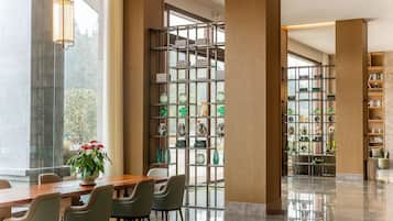 Un vestíbulo amplio con un mostrador de recepción de madera, asientos cómodos, una planta decorativa y un separador de vidrio con estantes de objetos decorativos.