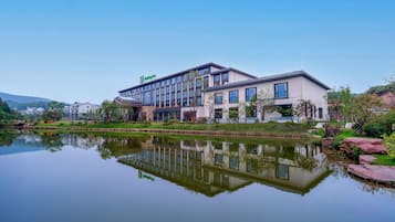 Un hotel moderno reflejado en el agua, rodeado de vegetación y un cielo despejado.