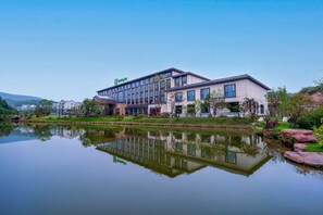 A modern hotel with a reflection in the water, surrounded by greenery and a clear sky. - Holiday Inn Jiuhua Mountain Hot Spring (Chizhou)