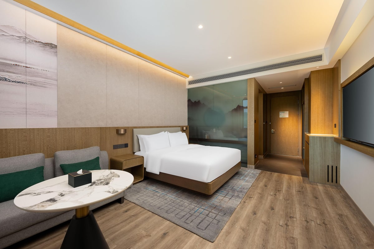 A modern hotel room with a bed, a sofa, a small table, and a TV.