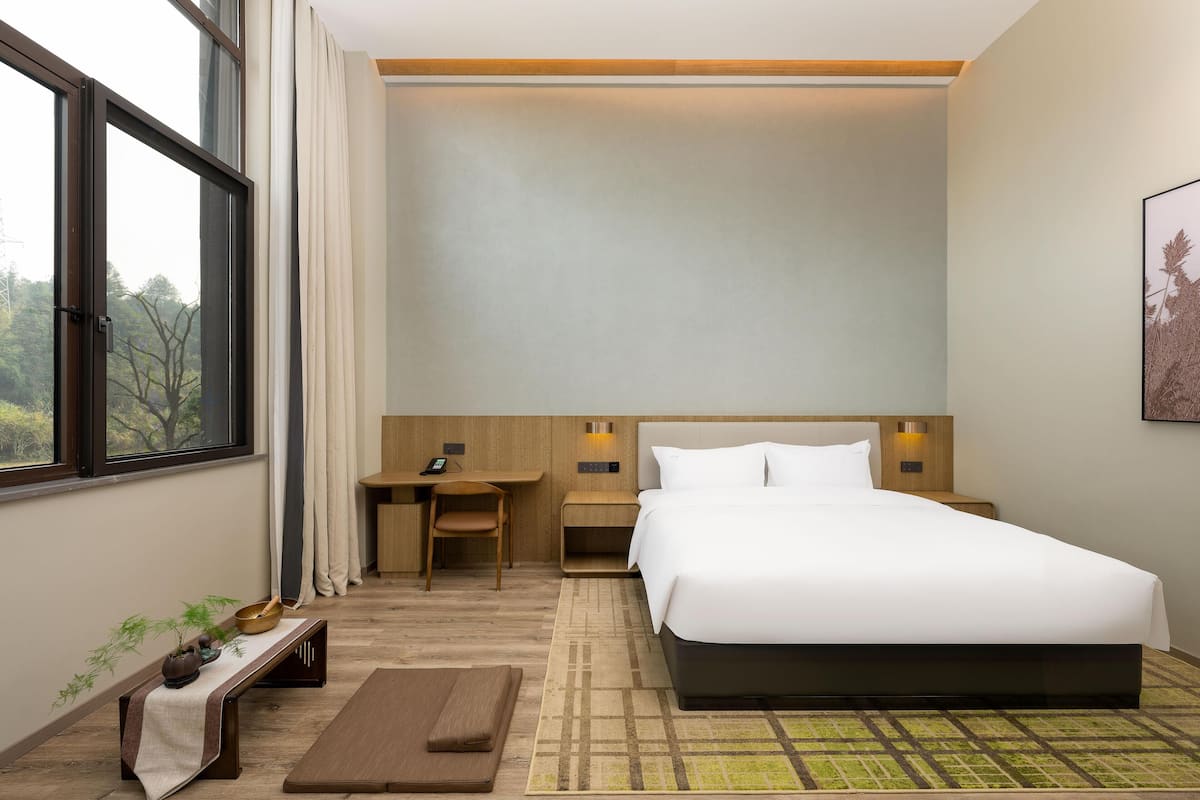 A hotel room with a large bed, a desk, a chair, and a small table with a plant.