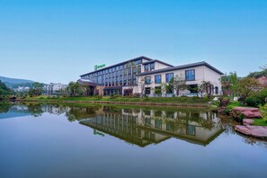 Ett Holiday Inn-hotell som speglas i vattnet, omgivet av grönska och en klar himmel.