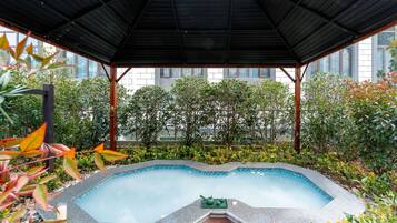 Piscina com borda azulejada, rodeada por vegetação e uma área coberta com telhado de metal.