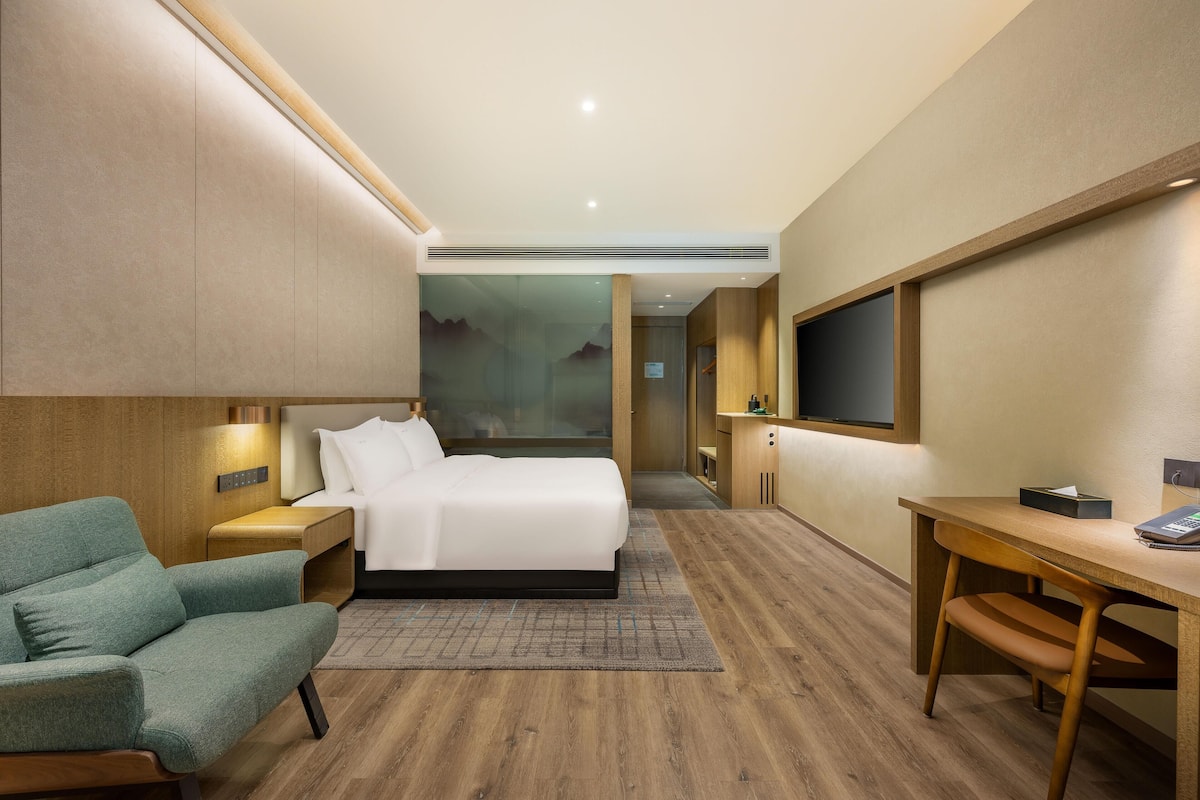 A modern hotel room with a bed, a desk, a chair, and a TV.