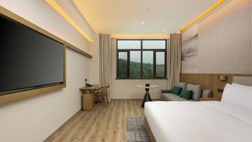 Habitación de hotel moderna con una cama grande, un escritorio con silla, una mesita y un amplio ventanal con vistas al exterior.