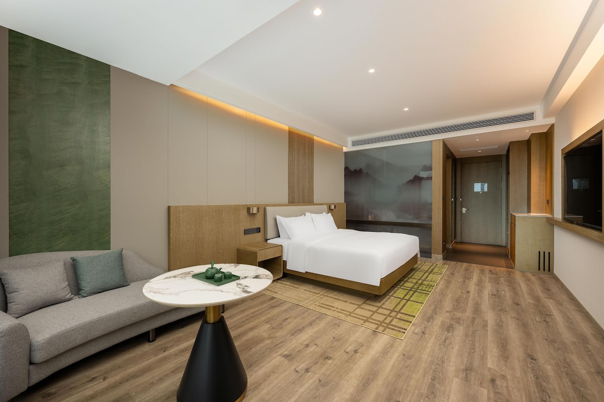 A modern hotel room with a bed, a sofa, a round table, and a TV.