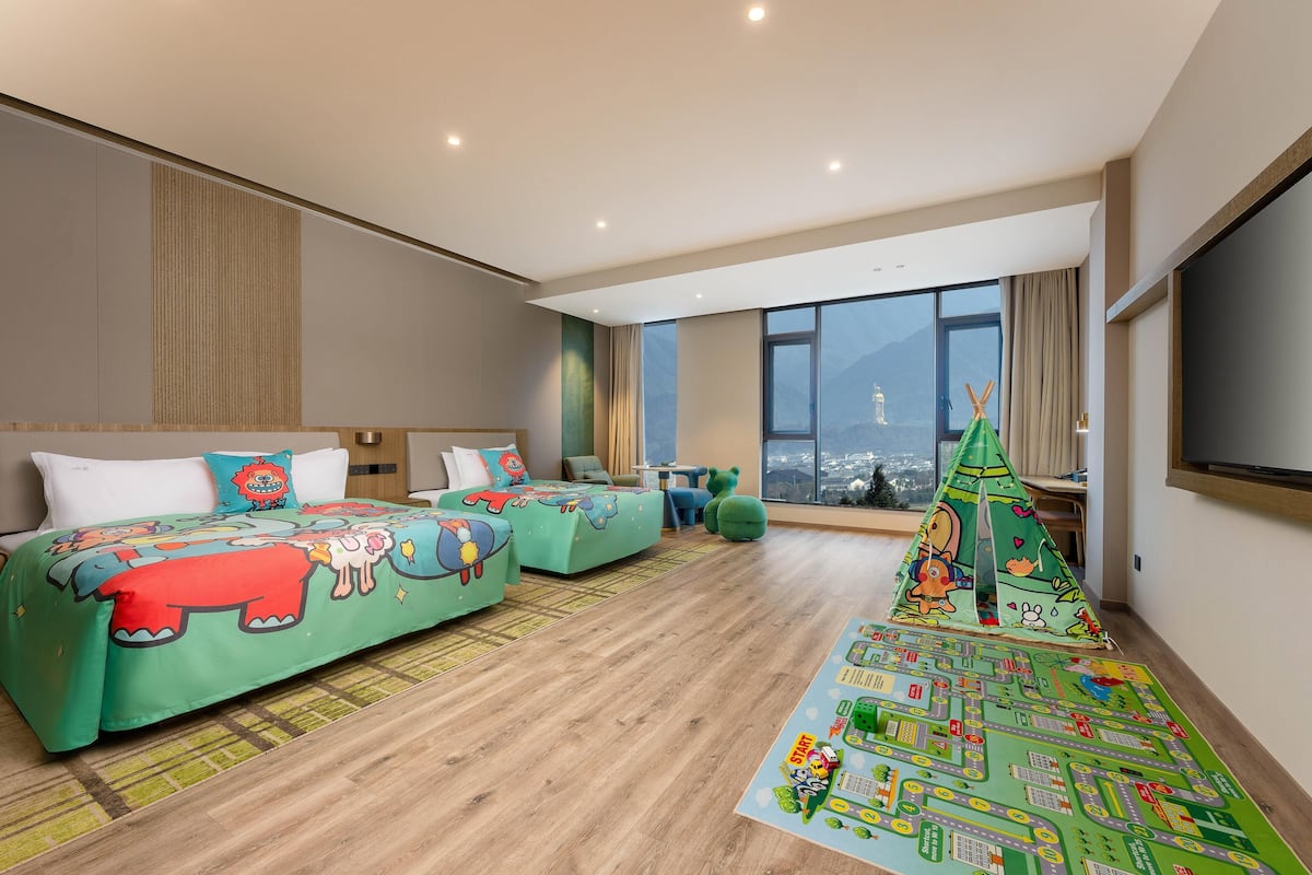 A modern hotel room with a large bed, a sofa, a play area, and a city view.