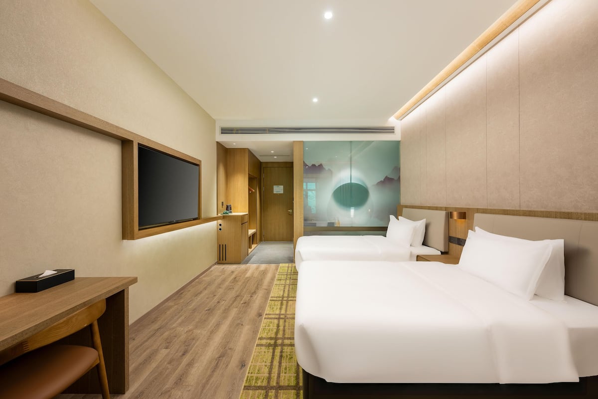 A hotel room with two beds, a desk, a TV, and a mural on the wall.