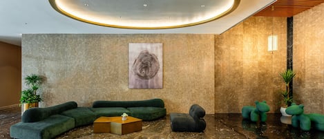 A lobby with a green sectional sofa, a small round table, and a potted plant.