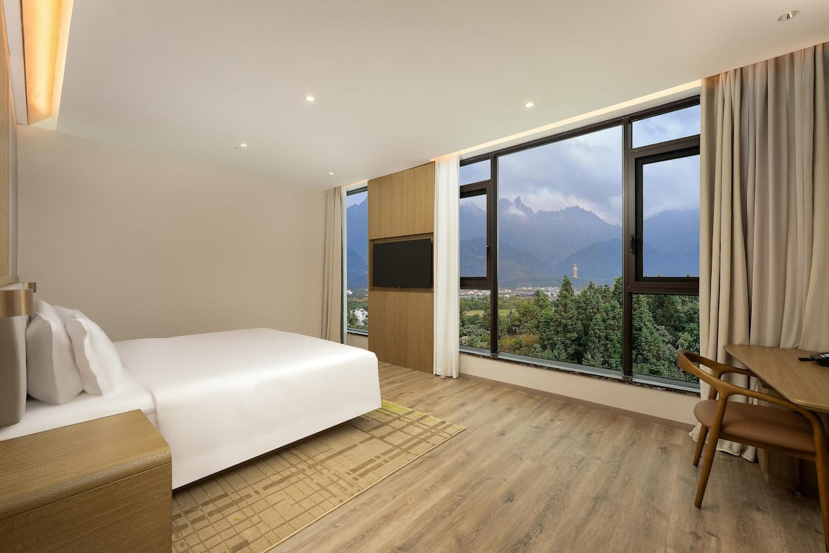 A hotel room with a bed, a desk, and a large window offering a mountain view.