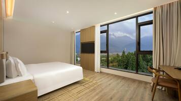 Habitación de hotel con cama, escritorio y ventana grande que ofrece vistas a la montaña.