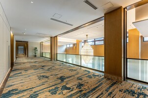 Un pasillo de hotel con alfombra estampada, barandales de vidrio y un candelabro.