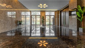 Un vestíbulo moderno con piso de mármol pulido, ventanas amplias y una exhibición de plantas en el centro.