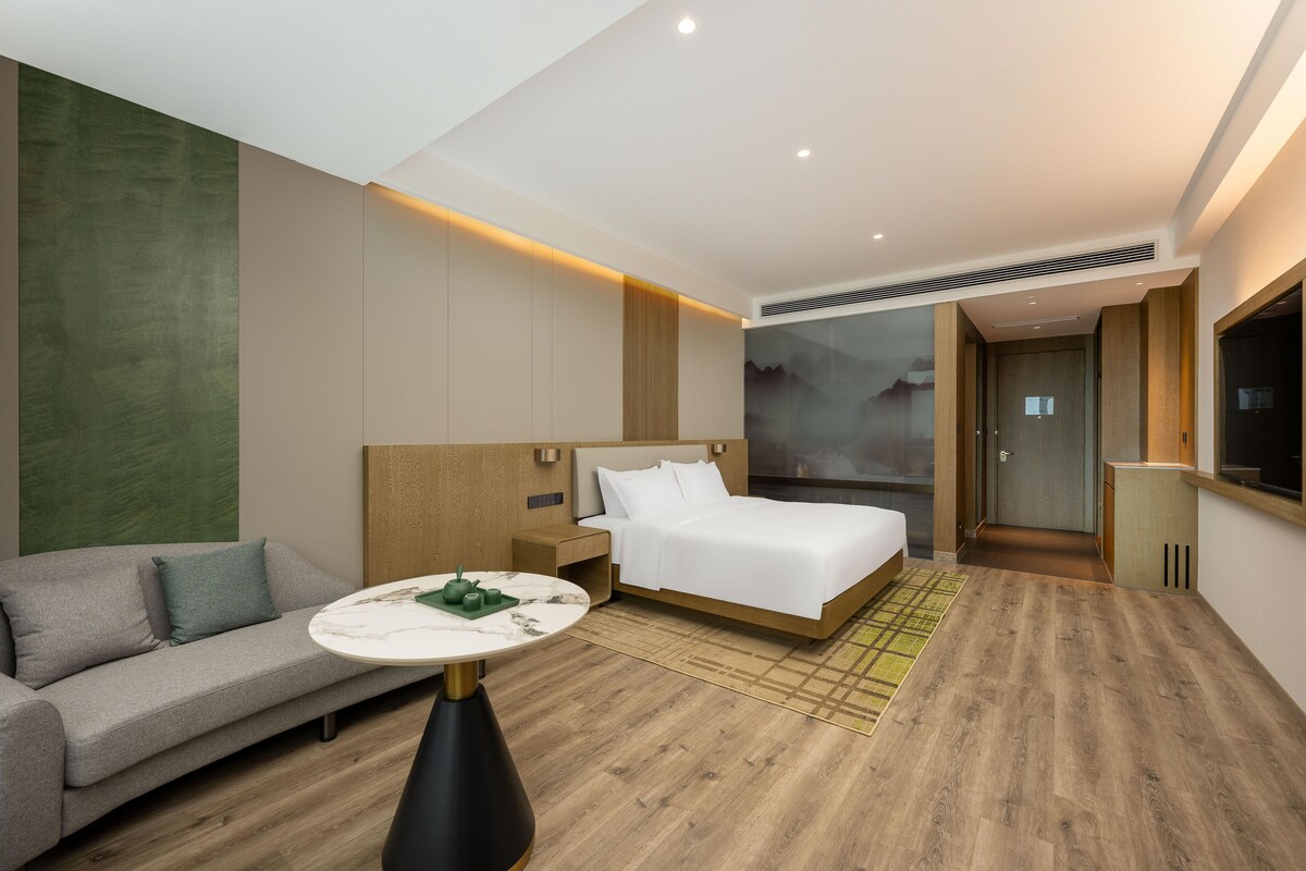 Quarto de hotel moderno com cama, sofá, mesa redonda e televisão.