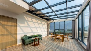 Una habitación espaciosa con techo alto, ventanas grandes, un sofá verde, una mesa de madera y vistas a montañas.