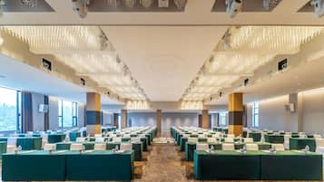 A conference room with rows of tables, ceiling lights, and large windows.