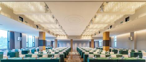 A conference room with rows of tables, ceiling lights, and large windows.