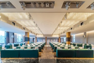 Un salón de conferencias con mesas dispuestas en filas, luces en el techo y ventanas amplias.
