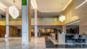 Um hall amplo com teto alto, lustres modernos, balcão de recepção e áreas de estar.