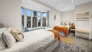 A modern hotel room with a large bed, a smaller bed, a desk, a chair, a wardrobe, and a view of the outside. - 4 Br & 4 Bath Cowley House Sleep 10 With Parking (Oxford)