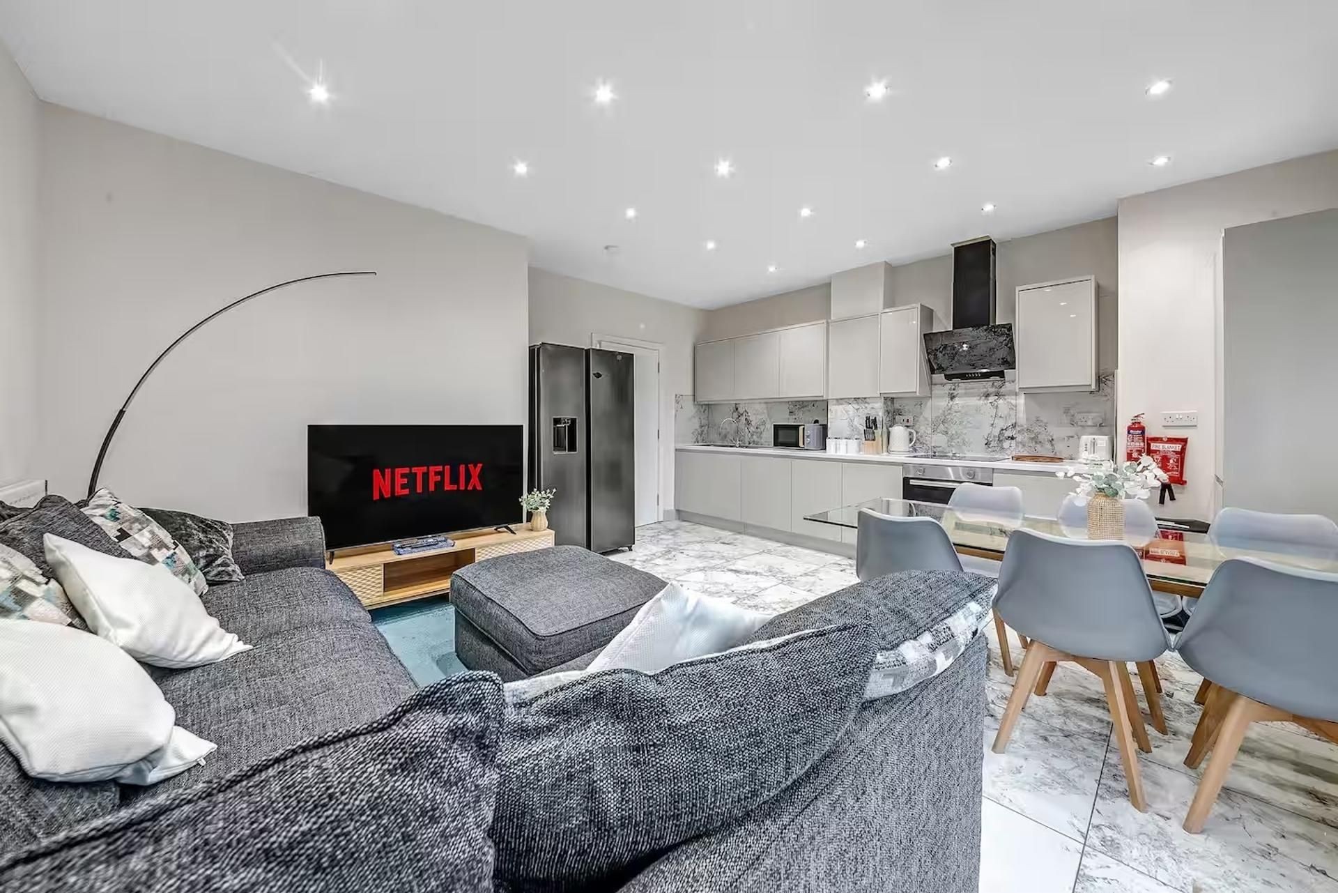 Un salon moderne avec un téléviseur à écran plat, un canapé gris et un coin repas comprenant des chaises et une table.
