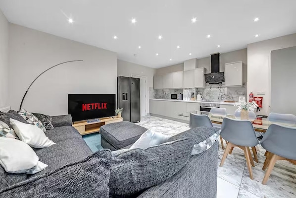 Una sala de estar moderna con un televisor de pantalla plana, un sofá gris y una zona de comedor con sillas y una mesa.