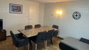 Una zona de menjador amb taula i cadires, un rellotge, una làmpada penjada a la paret i una porta.