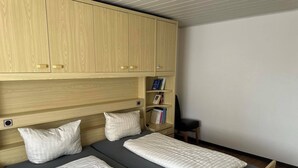 Una habitació amb dos llits, armaris de fusta, una biblioteca i una cadira.