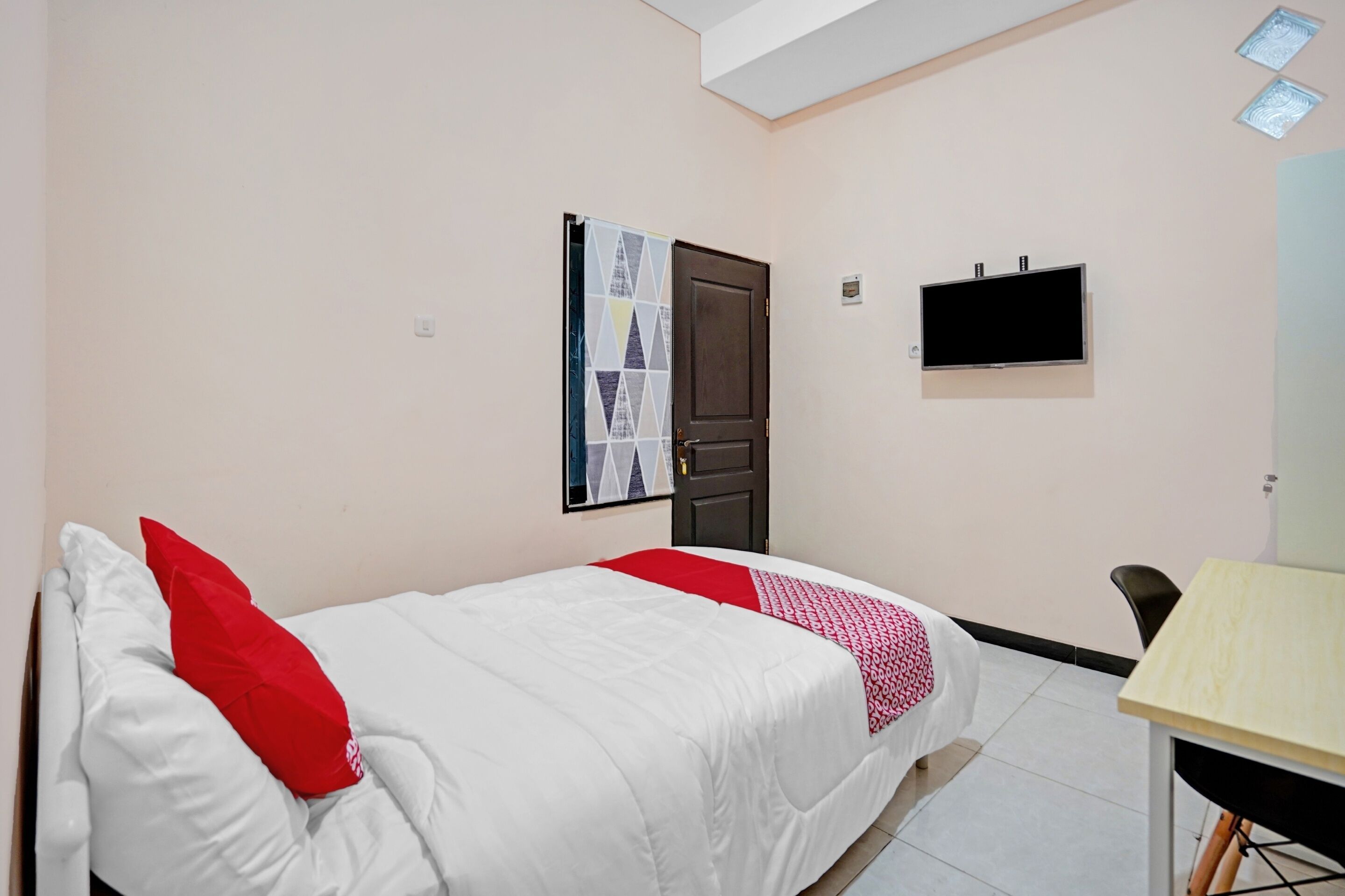 A bedroom with a bed, a desk, a TV, and a door.