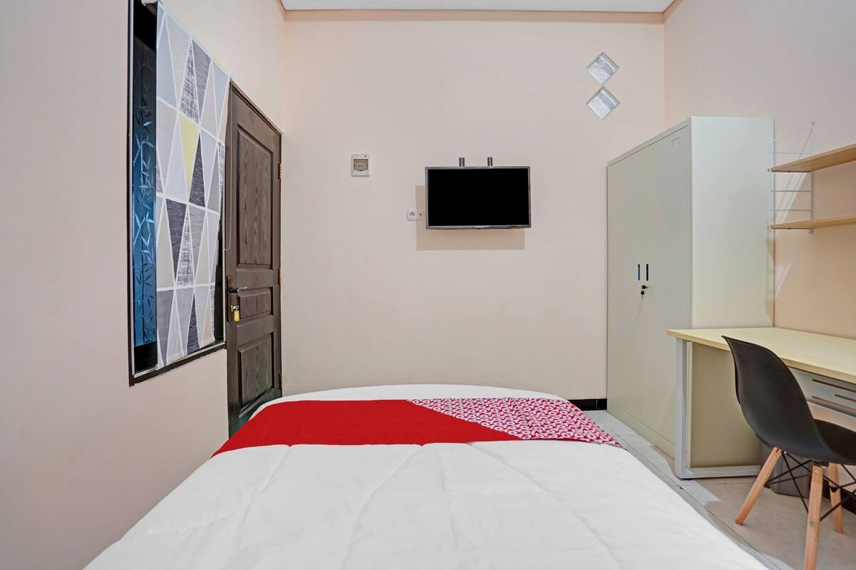 Une chambre à coucher avec un lit, un bureau, une chaise, une armoire et un téléviseur fixé au mur.