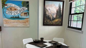 Un comedor con una mesa redonda, cuatro sillas blancas y un cuadro de un paisaje montañoso.