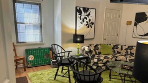 Un espacio habitable compacto con un sofá, dos sillones, una mesita, una lámpara y una alfombra con motivos deportivos.
