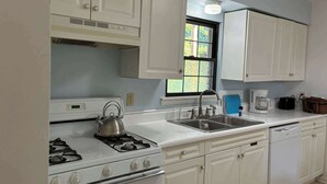 Una cocina con armarios blancos, una estufa a gas, un fregadero y una cafetera.