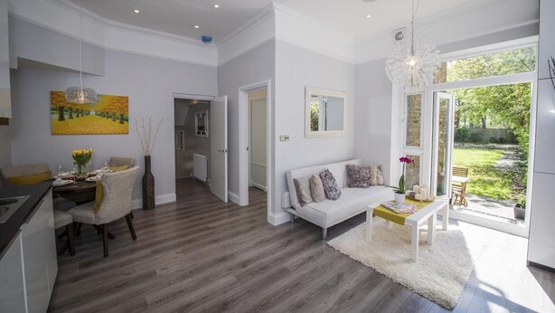 Eine moderne Küche mit grauen Schränken, ein Essbereich mit Tisch für zwei Personen, ein weißes Sofa und ein großes Fenster mit Blick auf den Garten.