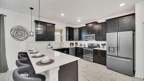 Una cocina moderna con armarios oscuros, electrodomésticos de acero inoxidable y una isla central con taburetes de bar.