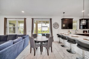 A modern kitchen with a dining area, a large window with curtains, and a view of the outdoors. - Gameroom | Pool & Spa | Waterpark | Near Disney 9008 (Davenport)