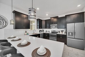 A modern kitchen with dark cabinets, stainless steel appliances, and a white island with placemats. - Gameroom | Pool & Spa | Waterpark | Near Disney 9008 (Davenport)