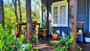 A wooden porch with a table and chairs, potted plants, and a window.