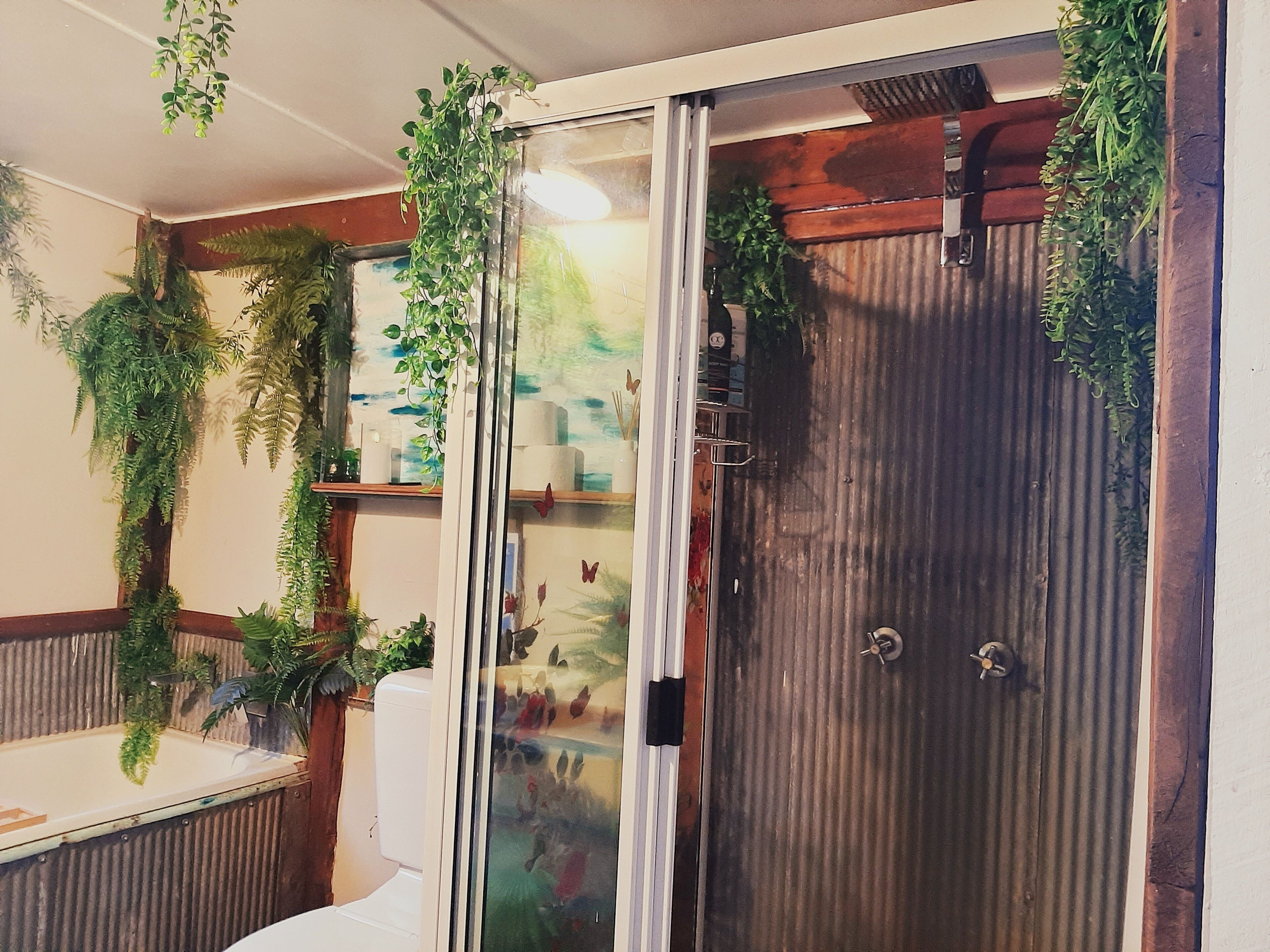 A bathroom with a glass shower door, wooden paneling, and various plants.