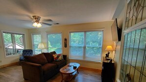 Ein geräumiges Wohnzimmer mit Deckenventilator, einer Couch, einem Couchtisch und großen Fenstern mit Jalousien.