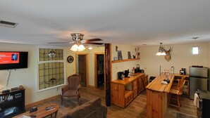 Ein geräumiges Wohnzimmer mit Holzboden, Fernseher, Kamin und Essbereich mit einer Holzbar und Stühlen.