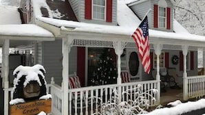 Ein schneebedecktes Haus mit Veranda, einer amerikanischen Flagge und einem Schild mit der Aufschrift 'Moonshine Creek'.