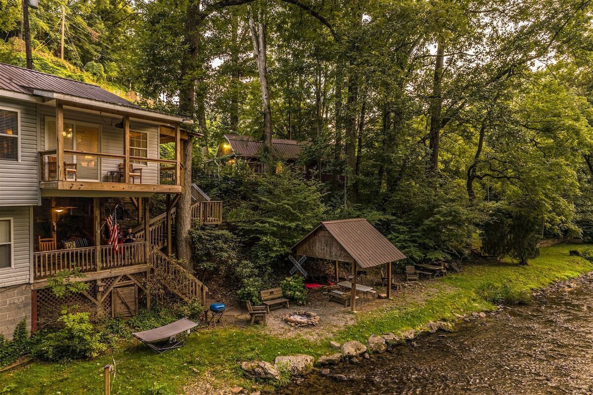 Une cabane avec une véranda, un petit abri de jardin et une rivière.