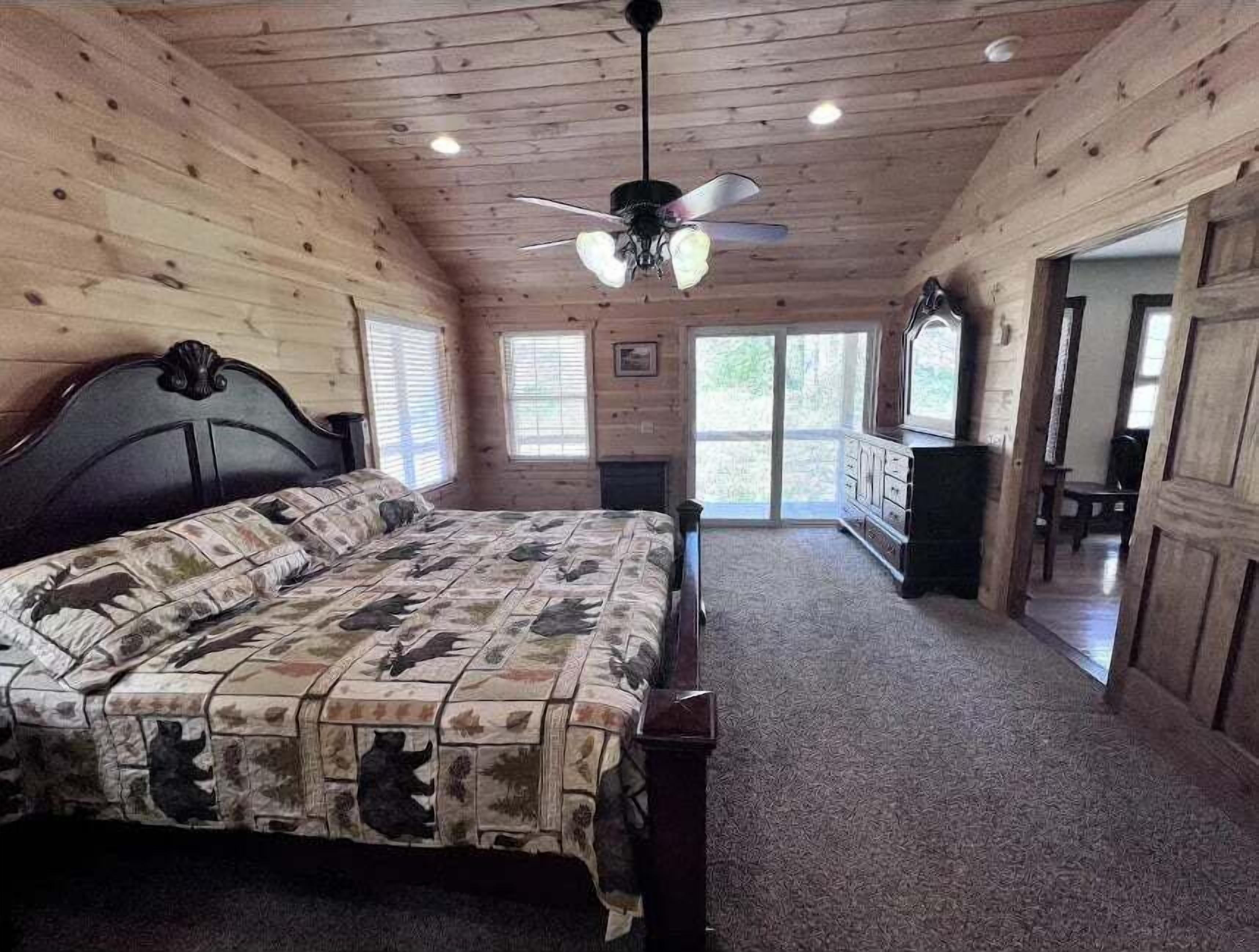 A bedroom with a bed, a ceiling fan, and a view of the outdoors through a sliding door.