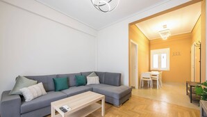 A modern living room with a grey sectional sofa, a wooden coffee table, and a dining area with a white table and chairs. - Stylish 2 Bd Urban Retreat Near Panormou Metro (Athina)
