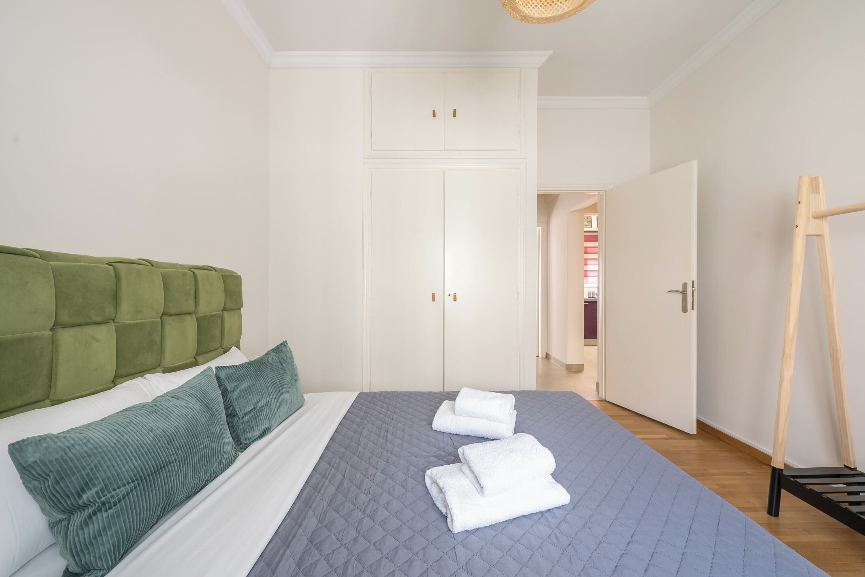 A neatly made bed with a green headboard, a grey quilt, and two white towels.