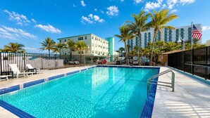 A swimming pool with a tiled edge, lounge chairs, palm trees, and a hotel building in the background. - Sand Vibes Studio Steps to Beach• Pool & Parking (Hollywood)