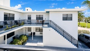 A modern two-story building with a covered outdoor seating area, a staircase, and a vehicle parked nearby. - Sand Vibes Studio Steps to Beach• Pool & Parking (Hollywood)