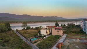 A riverside view with buildings and a road. - Yogamu India (Rishikesh)